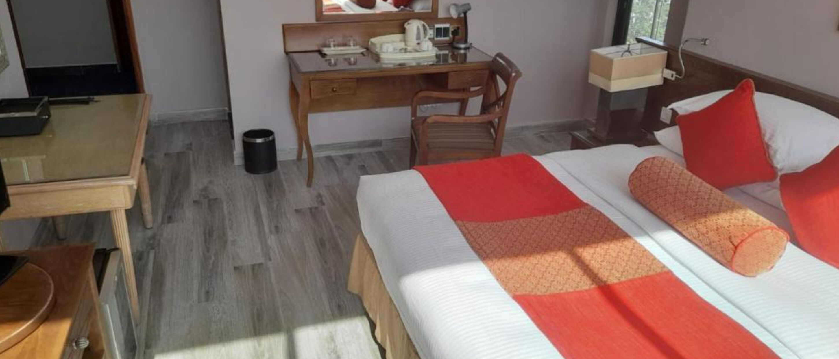 Une chambre d’hôtel avec un lit, un bureau, une chaise et une petite poubelle.