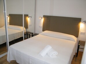 A hotel room with a bed, a mirror, a nightstand, and a wall-mounted light fixture.