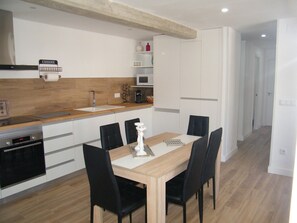 Una cocina moderna con encimera de madera, armarios blancos, horno empotrado y una zona de comedor con mesa y sillas.