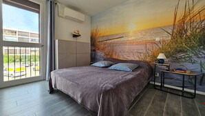 A bedroom with a large bed, a view of the outside, and a painting of a sunset on the wall.