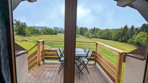 Une terrasse en bois avec une table et des chaises, donnant sur un champ verdoyant et des arbres.