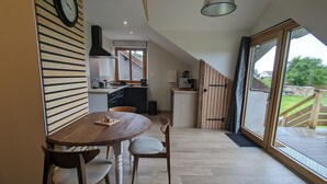 Une cuisine moderne avec un mur en bois, un coin repas avec une table et des chaises en bois, et une grande porte-fenêtre coulissante donnant sur une terrasse extérieure.