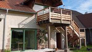 Une maison à deux étages avec un balcon en bois, une façade en pierre et une porte verte.