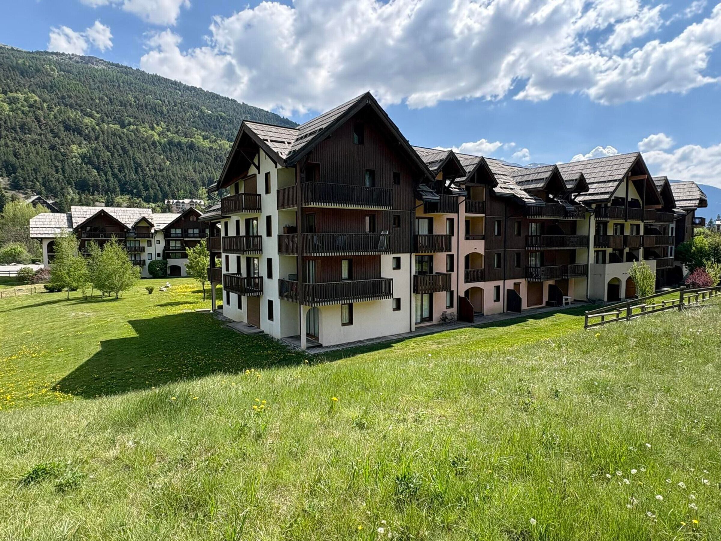 Un hôtel à plusieurs étages doté de balcons, d’une cour verdoyante et surplombant un paysage montagneux.