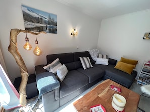 A modern living room with a dark grey sofa, patterned cushions, a wooden coffee table, and a unique light fixture.