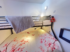A bunk bed with a floral bedspread, a towel hanging over the top bunk, and a red decorative item on the wall.