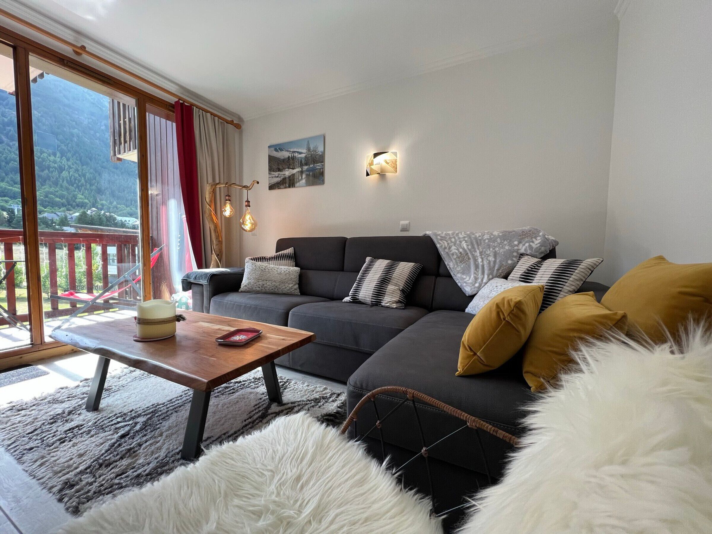 A living room with a sofa, a coffee table, and a rug. There is a window with a view of a mountain.