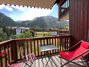 A balcony with a table and chairs, overlooking a mountainous landscape with houses.