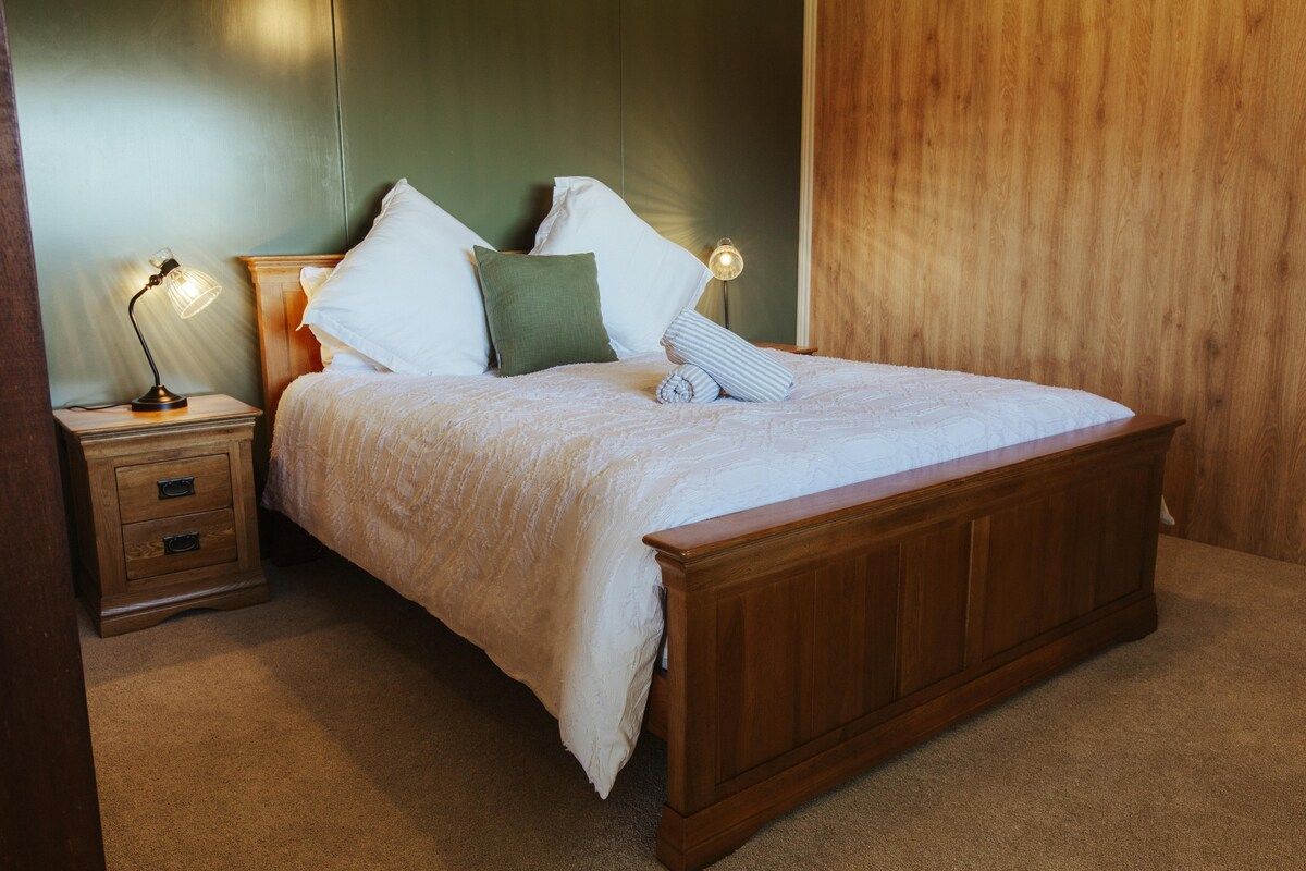 A neatly made bed with a wooden headboard and footboard, accompanied by two bedside tables with lamps.