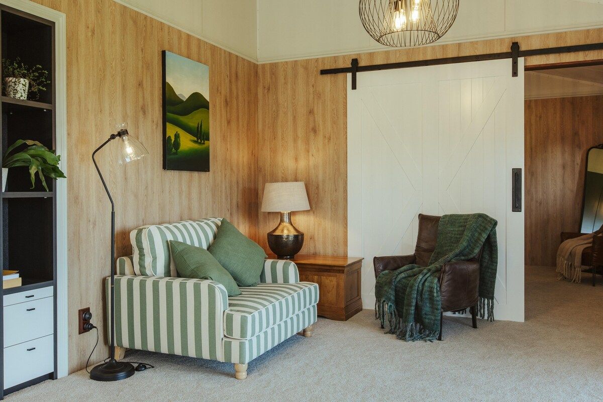 A room with a striped sofa, a lamp, a chair with a blanket, a bookshelf, and a painting on the wall.