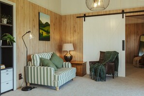 Una habitación con un sofá a rayas, una lámpara, una silla con una manta, una estantería y un cuadro en la pared.