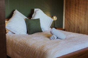 Una cama bien tendida con una colcha blanca y almohadas, una lámpara de noche y un cabecero de madera.