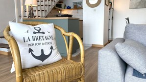 Een rieten stoel met een kussen met een nautisch ankerdesign, een grijze bank, een keuken met een magnetron, en een trap.