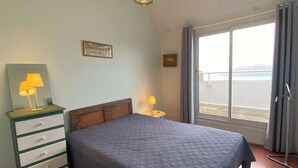 Een slaapkamer met een bed, een dressoir, een nachtkastje, een raam met uitzicht en een hanglamp.