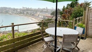 Een houten terras met een ronde tafel en stoelen, met uitzicht op een strand en stadsbeeld.