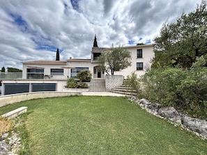 A two-story house with a balcony, a stone staircase, and a well-maintained lawn.