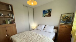A bedroom with a bed, a bookshelf, a painting, and a lamp.