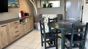 A compact kitchen with a dining area, featuring a round table and chairs, a sofa, and a flat-screen TV mounted on the wall.
