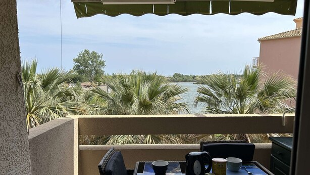A balcony with a table set for two, overlooking a body of water and palm trees.