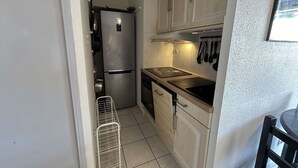 A compact kitchen with a stainless steel refrigerator, a black stove, and light-colored cabinets.