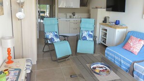 A compact living space with a kitchenette, a dining area with two chairs, a sofa, and a flat-screen TV.