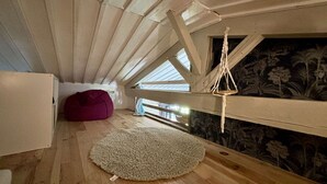 Une chambre à coucher de style loft avec des poutres en bois, un luminaire suspendu en macramé, un fauteuil poire rouge et un mur à motifs.