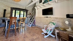 Un intérieur rustique avec une cheminée en pierre, des chaises en bois, un téléviseur et un ventilateur.