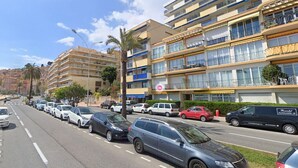 A multi-story hotel with balconies, a parking lot with various cars, and a clear sky.