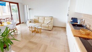 A modern living room with a sofa, coffee table, and chairs. There is a dining area with a table and chairs. The kitchen has a sink and a countertop.