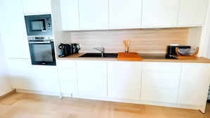 A modern kitchen with white cabinetry, a built-in oven, a coffee maker, and a wooden cutting board.