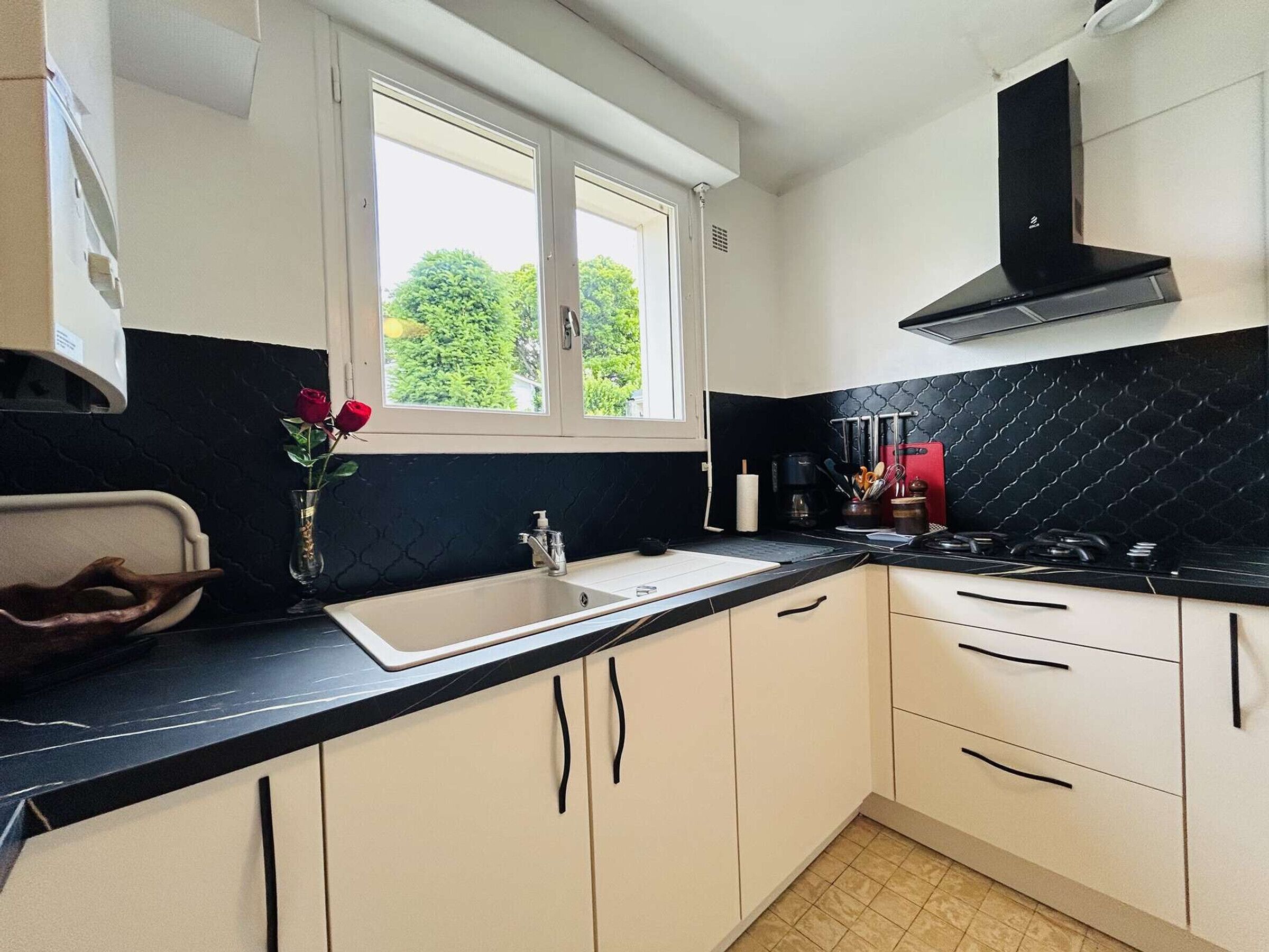 A kitchen with a window, white cabinets, a black countertop, and a stove.