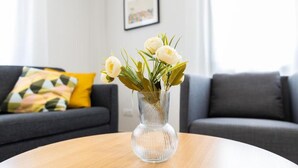 A clear glass vase with white flowers on a round wooden table in a living room.