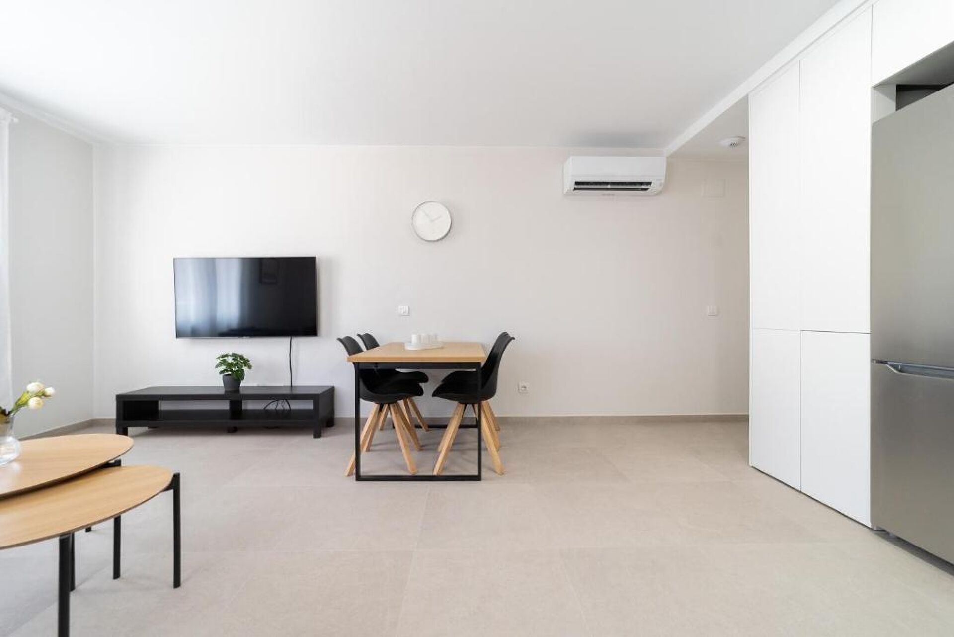 Una cocina moderna con refrigerador integrado, un comedor con mesa y sillas, un televisor de pantalla plana montado en la pared y un equipo de aire acondicionado.