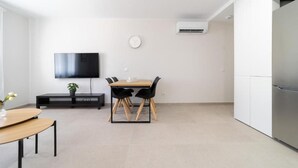 A modern kitchen with a built-in refrigerator, a dining area with a table and chairs, a flat-screen TV mounted on the wall, and an air conditioning unit.