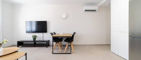 Una cocina moderna con refrigerador integrado, un comedor con mesa y sillas, un televisor de pantalla plana montado en la pared y un equipo de aire acondicionado.