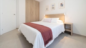 A bedroom with a bed, a nightstand, a wooden wardrobe, and three framed pictures on the wall.