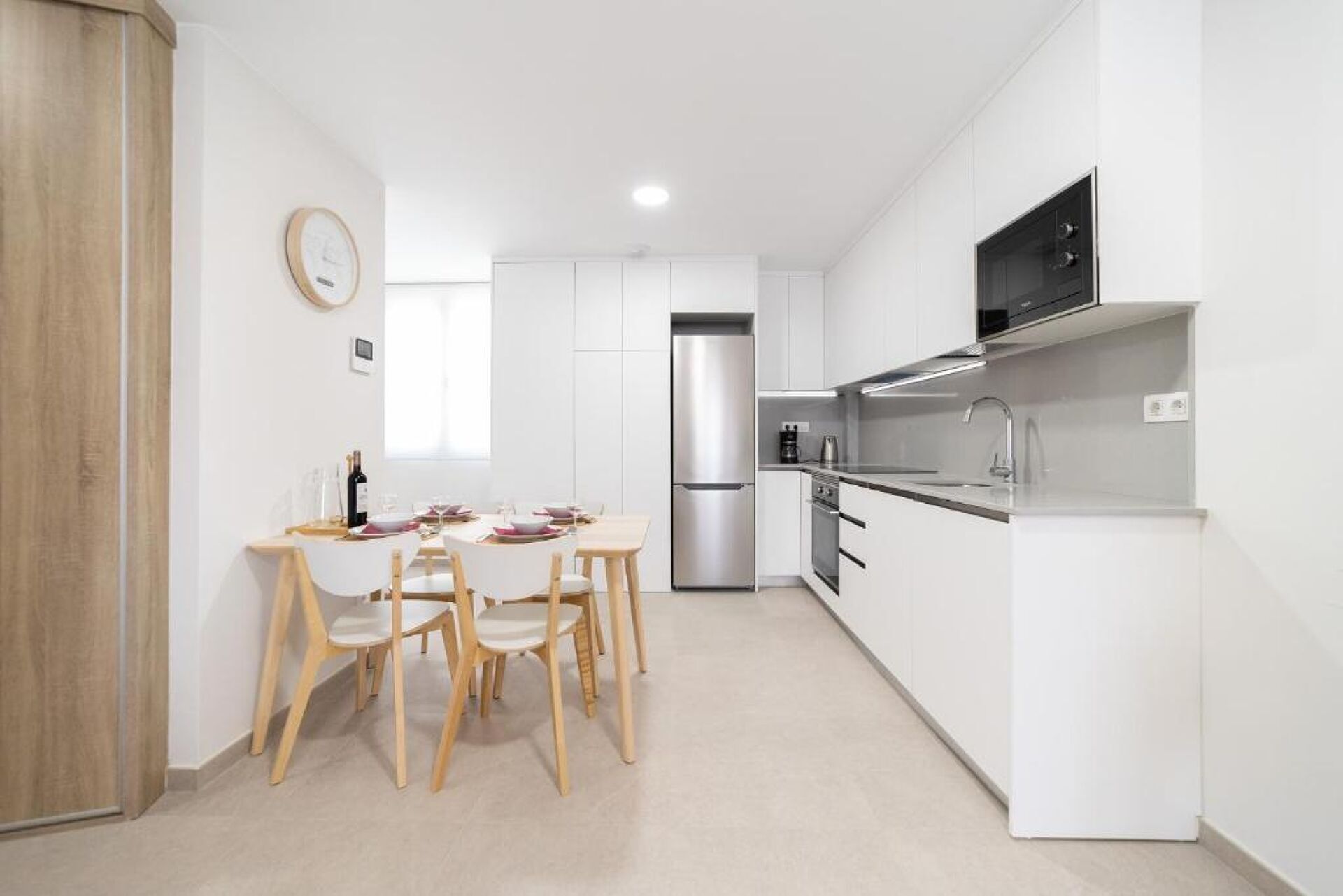 A modern kitchen with white cabinets, a stainless steel refrigerator, and a built-in oven.