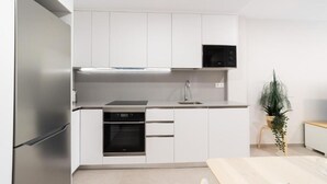Una cocina moderna con armarios blancos, un refrigerador de acero inoxidable, un horno empotrado y un microondas.