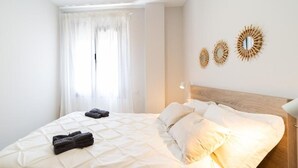 Una cama bien hecha con almohadas y toallas dobladas, una lámpara de noche y tres espejos decorativos montados en la pared.