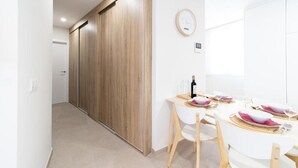 Un comedor con un armario de madera, un reloj de pared redondo y una mesa preparada para cuatro personas con sillas blancas.