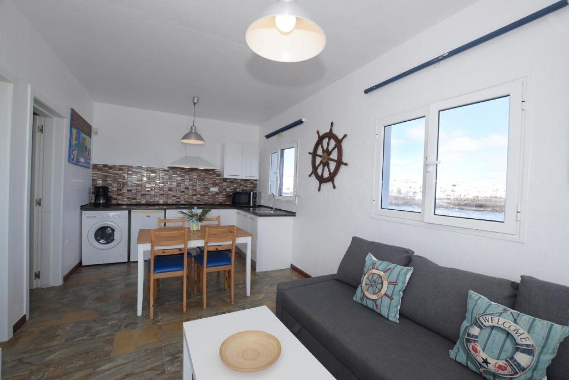 A compact living space with a kitchen, dining area, and a sofa with nautical-themed cushions.