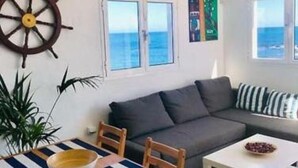A living room with a sofa, a dining table with chairs, a coffee table, a ship's wheel decoration, and a view of the sea through the windows. - Fischer Home Roque del Este (Punta Mujeres)
