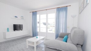 A modern living room with a grey sofa, a white coffee table, and a TV on a white cabinet. - Calma Suites La Garita B6 (Arrieta)
