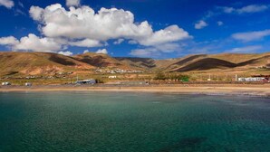 A coastal landscape with clear waters, a sandy beach, and rolling hills in the background.
