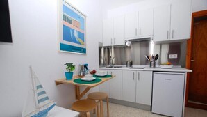 A compact kitchen with white cabinets, a stainless steel range hood, and a small refrigerator.