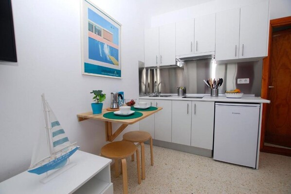 Una cocina compacta con armarios blancos, una campana extractora de acero inoxidable y un refrigerador pequeño.