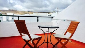 A rooftop terrace with two wooden chairs and a small round table.