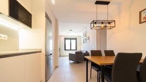A modern kitchen with a built-in oven and microwave, a dining area with a wooden table and chairs, and a living area with a sofa and a TV.