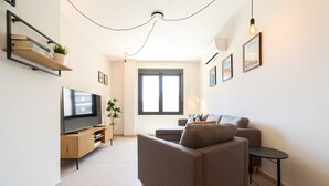 A modern living room with a sofa, a TV, a small table, and a window.