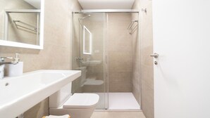 A modern bathroom with a glass-enclosed shower, a white sink, and a toilet.